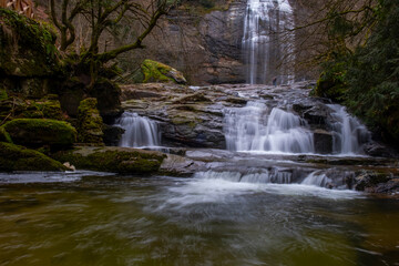 Obraz premium A serene view of Suuçtu Waterfall in Bursa, with water cascading over moss-covered rocks, surrounded by lush greenery and trees, creating a peaceful, natural landscape perfect for nature lovers.