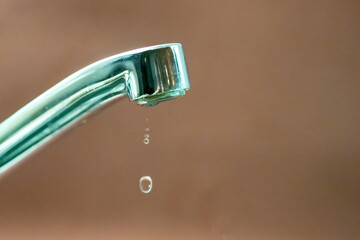 Leaking faucet dripping water droplets on brown background