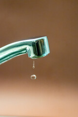 Leaking faucet dripping water droplets on brown background