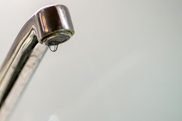 Leaky faucet dripping water, close-up, shiny metal