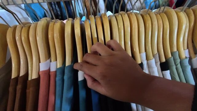 First person POV clip of a hand buying clothes from a collection of clothes hanging in a hangar. POV videography of sorting clothes in a mall in Indonesia in 4K HD resolution.