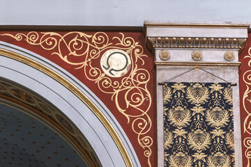 Decorative architectural detail in the Church of Saint Nicholas in Ermoupolis, Syros, Greece, featuring intricate gold scrollwork on a red background and a circular emblem