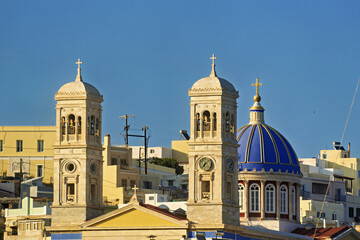 Naklejka premium Church of Saint Nicholas in Syros, Greece, featuring a large blue dome topped with a golden cross. The dome sits above a red and white drum with tall arched windows