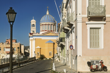 Obraz premium Church of Saint Nicholas in Syros, Greece, featuring a large blue dome topped with a golden cross. The dome sits above a red and white drum with tall arched windows