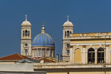 Obraz premium Church of Saint Nicholas in Syros, Greece, featuring a large blue dome topped with a golden cross. The dome sits above a red and white drum with tall arched windows
