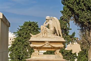 Obraz premium Marble angel statue in the Orthodox Cemetery of Ermoupolis, Syros, Greece, seated on an ornate pedestal with one hand resting against its head in a contemplative pose.