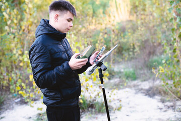 Young man playing a kalimba outdoors, with a microphone setup, capturing sounds in nature. A creative and modern approach to music production and hobby in a serene setting.