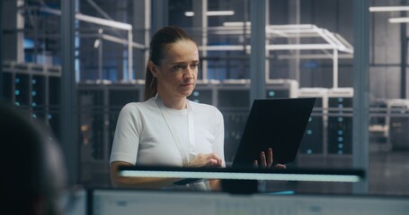 Mobile IT Management, Focused Female IT Professional Standing and Actively Working on Thin Laptop....