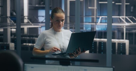 Experienced Female Engineer Uses Portable PC Run Diagnostics Performance Metrics in Bright, Secure Data Center Environment. Concept On Site Troubleshooting, IT Expertise, and Infrastructure Integrity.