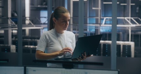 Experienced Female Engineer Uses Portable PC Run Diagnostics Performance Metrics in Bright, Secure Data Center Environment. Concept On Site Troubleshooting, IT Expertise, and Infrastructure Integrity.