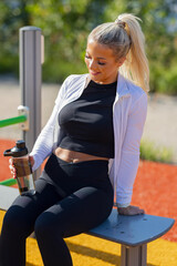 Woman resting outdoors after workout holding water bottle on sunny day