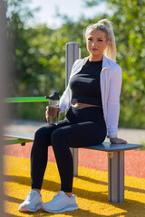 Woman resting at outdoor fitness park holding water bottle after workout