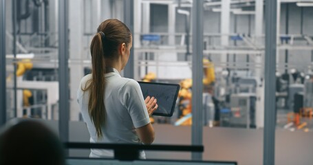 Female Engineer Managing Production Via Tablet. Woman Standing and Operating Digital Device. Clear Background Shows Automated Machinery and Robotics of Smart Factory. Mobile Control, Industry 4.0. © Framestock