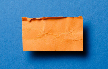 One single orange torn ripped wrinkled crumpled blank paper note with drop shadow, folded edge and copy space for text on blue background
