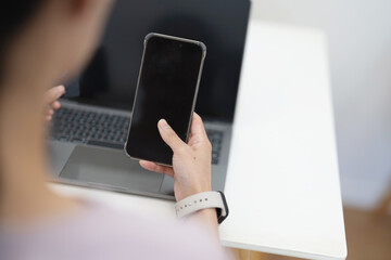 A person using a smartphone while sitting at a desk with a laptop.
