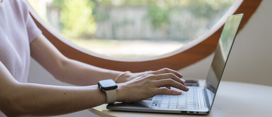 A person typing on a laptop in a bright, modern workspace with a large circular window.