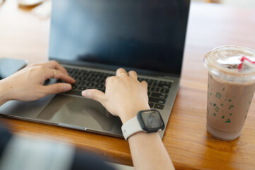 Person typing on a laptop beside a beverage on a wooden table.