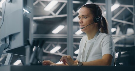 Specialist Manages Network Systems From Workstation in Network Operations Center. Woman Wearing Professional Headset Coordinate Tasks. Proactive System Monitoring and Coordinated Digital Operations.