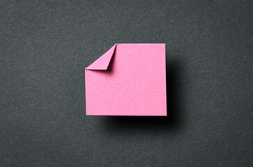 Pink paper note cardboard with folded corner dog-ear earmark, shadow and copy space for text on black gray background