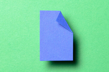 Blue blank paper note cardboard with folded corner dog-ear earmark, shadow and copy space for text on green background