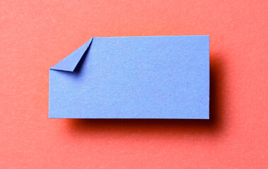 Blue blank paper note cardboard with folded corner dog-ear earmark, shadow and copy space for text on red background
