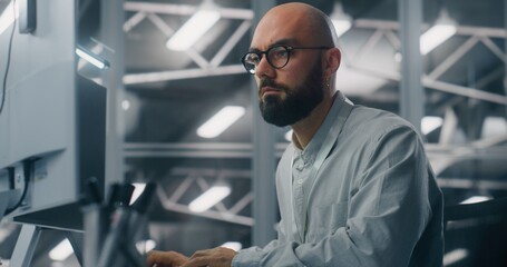Bearded Male IT Specialist With Glasses, Intensely Focused on Computer Monitor. Background Features Cool, Technical Environment of Server Control Room. Critical Data Analysis and Dedicated Expertise.
