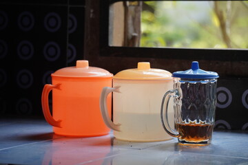 Three cups with lids and a glass of tea on a table.
