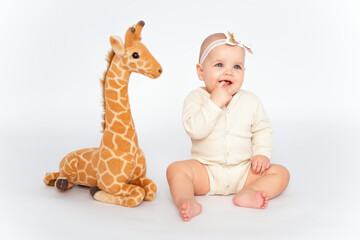 a baby on a white isolated background with a stuffed giraffe toy, a small child girl in light clothes, a place and space for text and advertising