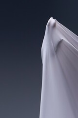 A human hand presses against taut white fabric, creating an abstract, sculptural form against a dark gray background.