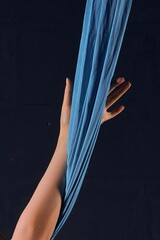 Graceful female hand grasping blue aerial silk against a dark background
