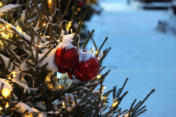 A New Year's tree with toys and garlands stands outside under the snow.