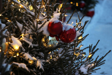 A New Year's tree with toys and garlands stands outside under the snow.