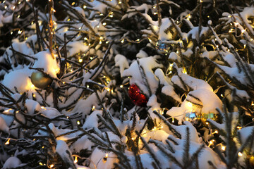 A New Year's tree with toys and garlands stands outside under the snow.