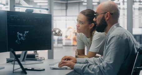 Focused Specialists Monitoring Factory Automation Work. Male and Female Technical Specialist Monitoring Real Time Factory Automation on Dual Screen Workstation. Process Control, Technical Oversight.