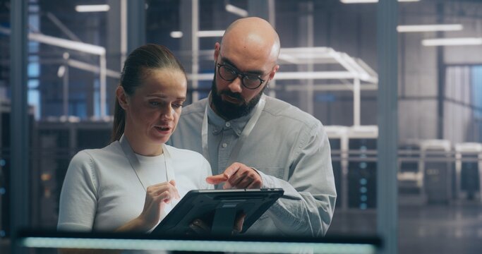 Male and Female IT Engineer Team Collaborating and Discussing Data Displayed on Digital Tablet, Standing in Secure, High Tech Environment of Data Center. Concept Teamwork and Mobile System Diagnostic.