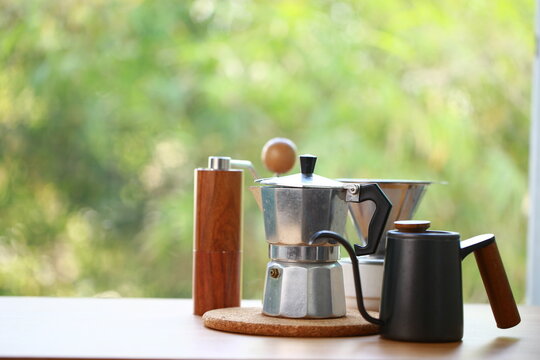 Coffee set with coffee grinder, jug, moka pot and brewer on wood table with green nature as background.