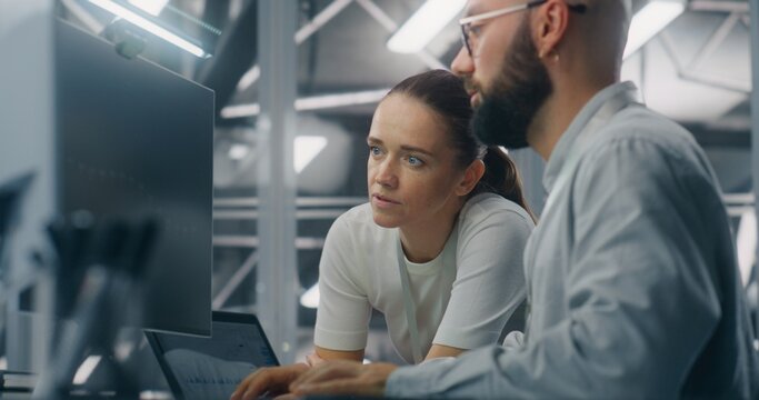 Engineers Reviewing Network Performance Data. Male and Female IT Engineer Team Collaborating Over Computer Monitor to Review Critical Network Performance Metrics. Teamwork and Real Time IT Monitoring.