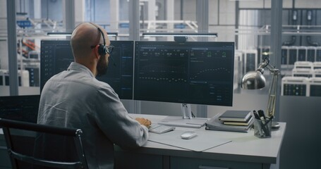 Cloud System Monitoring, Engineer on Headset Analyzing Performance Metrics, Working Two Monitors and Tablet. Screens Display Complex Cloud System Metrics and Graphs on Backdrop of Large Server Hall.