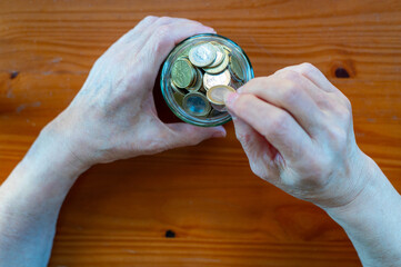 Hands Placing Coins Into Glass Jar For Saving Money And Personal Finance Concept