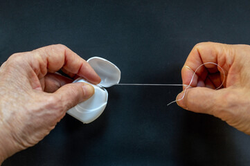 Hands pulling dental floss from plastic dispenser over dark background