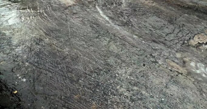 Close up of rainwater flowing over wet asphalt street surface during rain.( slow motion )
