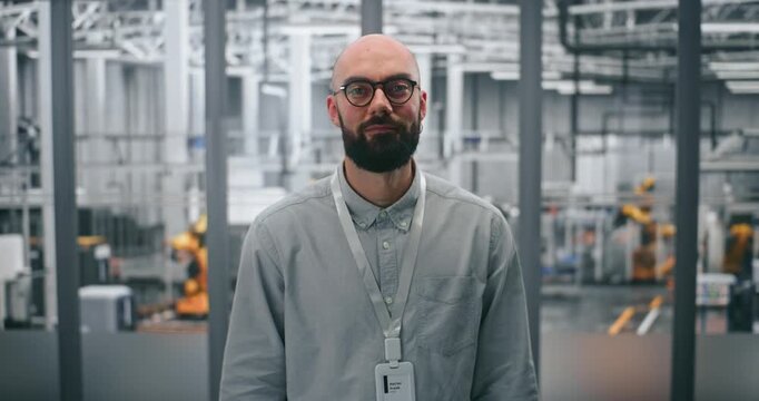 Bearded Engineer With Glasses, Looking Directly With Professional Demeanor. Man Standing in High Tech Environment of Modern Manufacturing Facility. Technical Expertise and Innovation in Industry 4.0.