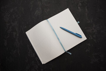 An open notebook with blank pages and a blue pen placed on a dark textured surface. Ideal for writing, planning, or note-taking.