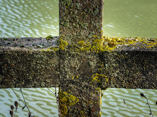 Weathering stone cross with moss and lichen over water