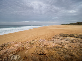 Wide sandy beach with Atlantic Ocean waves and rock formations