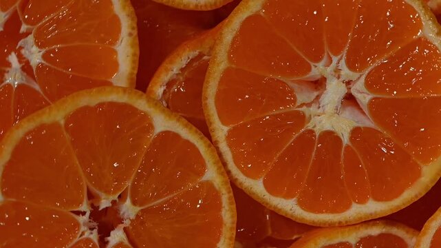 A vibrant seamless 4K video loop of fresh mandarin slices rotating on a dark surface, captured from a top-down view. The clip highlights the bright orange color, juicy segments, and glossy texture of 