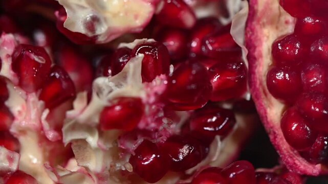 A vibrant seamless 4K video loop of fresh pomegranate slices and clusters rotating on a dark surface, filmed from a top-down perspective. The clip showcases the brilliant ruby red seeds, juicy texture