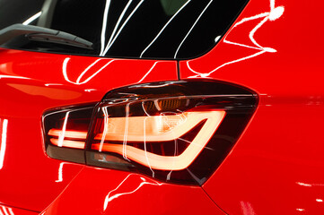 LED turn signal in the rear brake light of the red car. Modern car lantern, close-up. Detail on the rear light of a red glossy car. Close-up of a modern red automobile with LED red taillights.