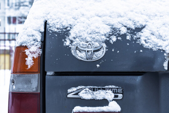 Toyota logo covered with snow. A gray Toyota Land Cruiser covered with snow is parked on the street. Snow-covered Land Cruiser 80 (J80) logo on the trunk lid in winter. Japanese SUV car. 