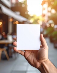 Hand Holding Blank White Square Card Outdoors with Bokeh Lights.